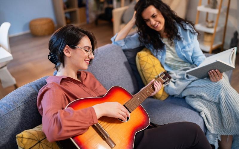 a person playing a guitar next to a person sitting on a couch